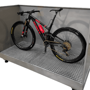 Rower górski typu full suspension z czarną ramą i czerwonymi akcentami, stojący na metalowej kratce w specjalnej myjni. Widoczny złoty łańcuch i kaseta.