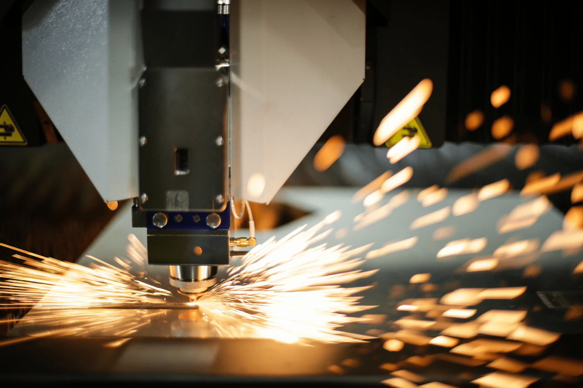 Praca maszyny do cięcia laserowego metalu ze snopem iskier. Gorące, jasne, złote iskry rozprzestrzeniają się po powierzchni.