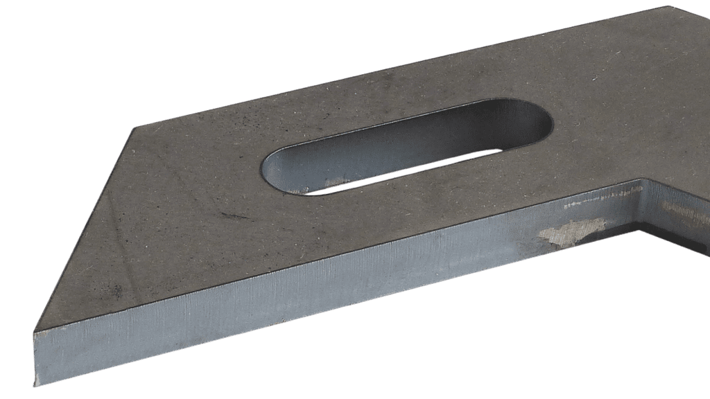 Zbliżenie na metalowy płaskownik, częściowo zardzewiały, z podłużnym otworem. Widoczne ślady zużycia.
