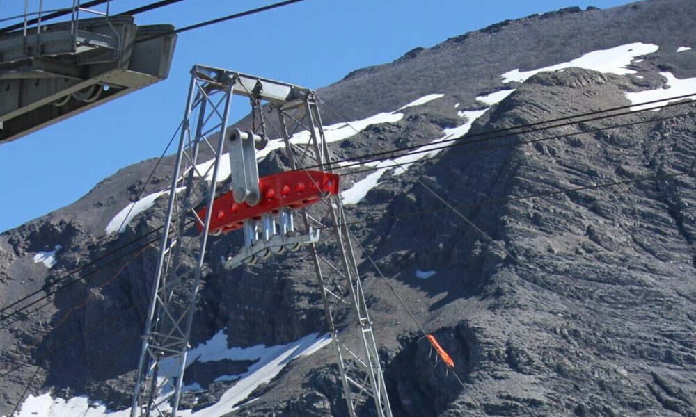 Elementy wyciągu narciarskiego na tle skalistych gór pokrytych śniegiem w słoneczny dzień.