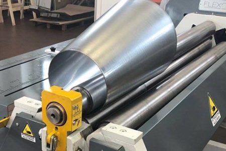 Specjalistyczna maszyna do zwijania blachy stożkowej, tworząca precyzyjny element metalowy w zakładzie produkcyjnym. Widoczne walce i gotowy stożek.