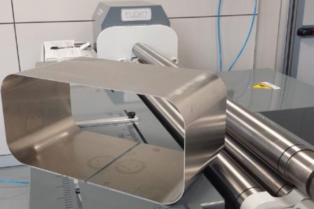 Blat stołu roboczego maszyny FLEXO z wygiętą metalową rurą o prostokątnym przekroju i metalowymi rolkami.